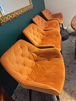 Four burnt orange microfiber dining chairs aligned, shows upholstery and legs