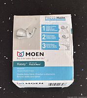 Retail box front displaying Moen Kasey Press & Mark robe hook details