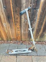 Full view of Razor scooter upright against wooden fence