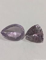 Two faceted amethyst gemstones, pear and trillion cuts, pale lavender color