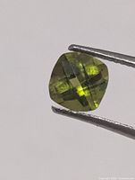 Square cushion faceted green peridot held by tweezers