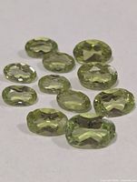 Eleven faceted green peridot gemstones arranged on white background