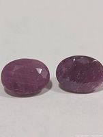 Two oval faceted rubies side by side on white background