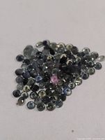Pile of small round faceted sapphires in blue-green hues with one pink stone