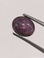 Close-up of purplish-red star ruby held by tweezers
