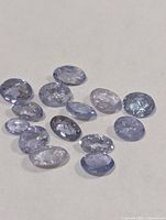 Cluster of thirteen loose oval tanzanite gemstones on neutral background