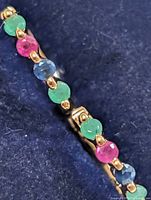 Close-up of gemstones on hoop earring showing alternating green, pink, blue stones