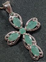 Front view of silver cross pendant showing emerald arrangement and bail