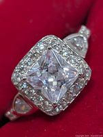 Close-up of ring face showing princess-cut center stone, halo and shoulder design