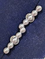 Close-up of one silver bead-link earring on dark fabric