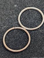 Two small silver-tone continuous hoop earrings on dark background