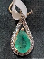 Front view of silver pendant with emerald center and topaz halo