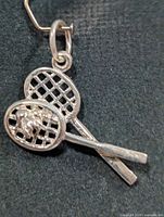 Front view of silver pendant showing crossed tennis rackets and ball detail