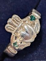 Front view of silver Claddagh ring showing heart, crown, hands and green stones