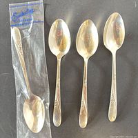 Front view of four sterling silver teaspoons, one in original Easterling plastic sleeve