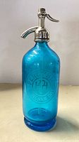 Full front view of blue glass soda siphon bottle showing etched Percy Hill crest