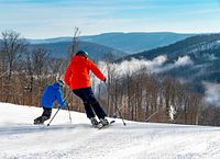 Two skiers on groomed slope with mountain backdrop