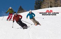 Skiers descending snowy slope with Mount St. Louis Moonstone branding