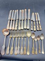 All 23 flatware pieces laid out — 12 knives, 6 forks, 1 ladle, 1 tablespoon, 3 teaspoons