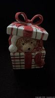 Front view showing teddy bear face peeking from gift box with ribbon lid