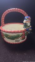 Front view of Fitz & Floyd ceramic basket showing handle, evergreen garland and attached elf nutcracker figure