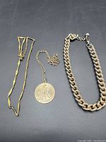 Overview of three gold-tone necklaces on black background