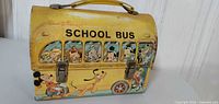 Front side of yellow Disney school bus lunchbox with handle and latch