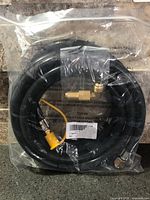 Sealed package containing coiled black propane hose with attached brass fittings and separate elbow adapter