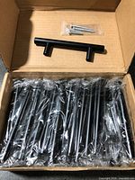 Open box showing multiple individually wrapped black metal T-bar pulls and bagged screws