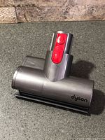 Top view of Dyson vacuum head showing grey housing, red release button, Dyson branding
