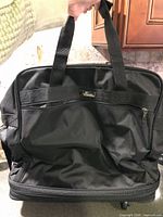 Front view of black rolling duffle showing carry handles and front zip pocket