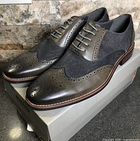 Side view of both shoes on box showing leather and fabric uppers, brogue detailing