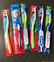 Six sealed toothbrushes laid out showing brands and colors