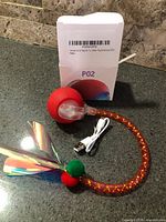 Ball toy, feather tail, USB cable and box on countertop