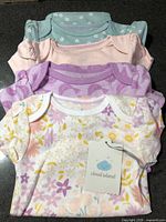 Stack of four Cloud Island bodysuits showing assorted prints and attached tag