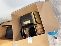 Cardboard box containing stacks of sleeveless and sleeved 7" singles plus black plastic storage box