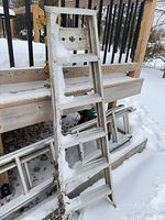Full view of aluminum 4-step ladder leaning against deck in snow
