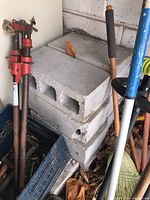 Stack of four hollow concrete blocks with garden tools nearby