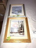 Both framed paintings stacked on bed showing overall view