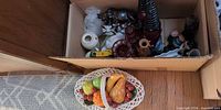 Cardboard box showing assortment of glassware, figurines, wood carving, decanter, vase, cordial glasses