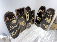 All six lacquer panels leaning against wall showing variety of gilt and inlay scenes, sizes similar