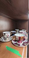 Six assorted Shafford teacup and saucer sets on shelf