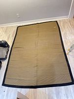Full view of tan woven rug with black border