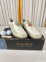 Shoes on original FootJoy box with two golf balls and tube of tees visible