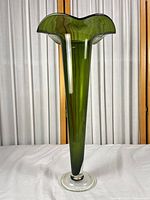 Full view of tall olive green trumpet glass vase on clear foot