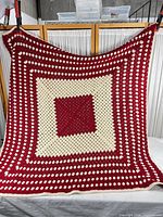 Full view of square red and cream granny-square afghan hanging from clips