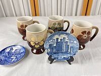 Lot overview showing four mugs, two plates, stand