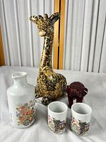 Full view of all five items: sake bottle, two sake cups, resin elephant, ceramic giraffe