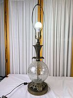 Full view of brass and crackle glass table lamp illuminated, no shade
