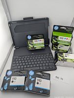 Front view: Logitech Slim Folio keyboard case opened with six sealed HP 910 ink packs arranged around it